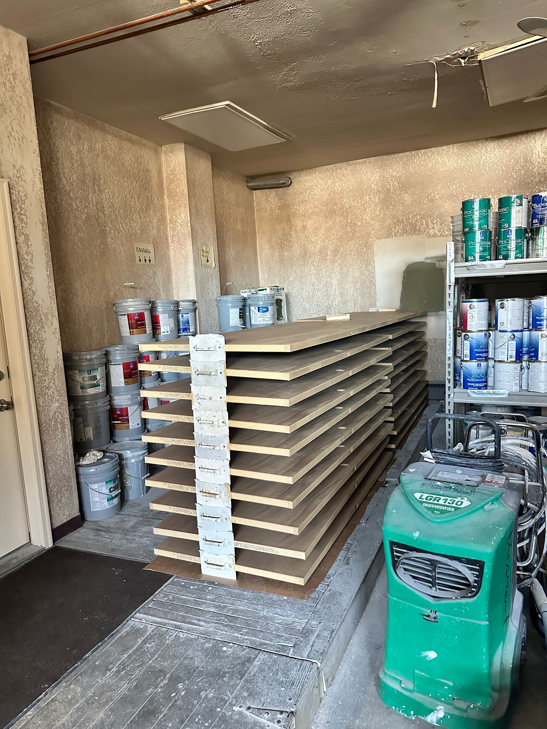 A room filled with buckets of paint and a green air compressor.