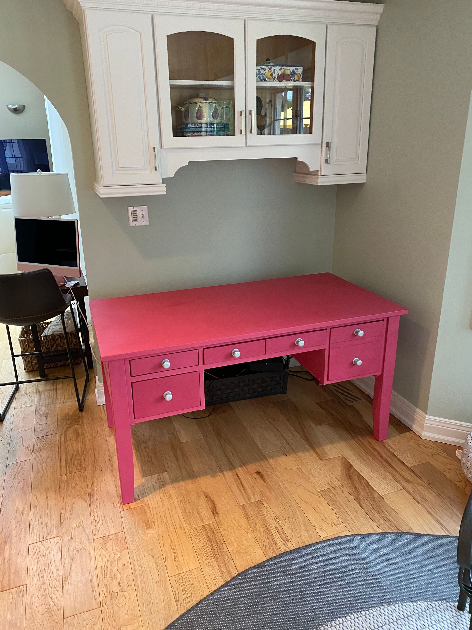 A pink desk with drawers and a white cabinet above it in a living room.