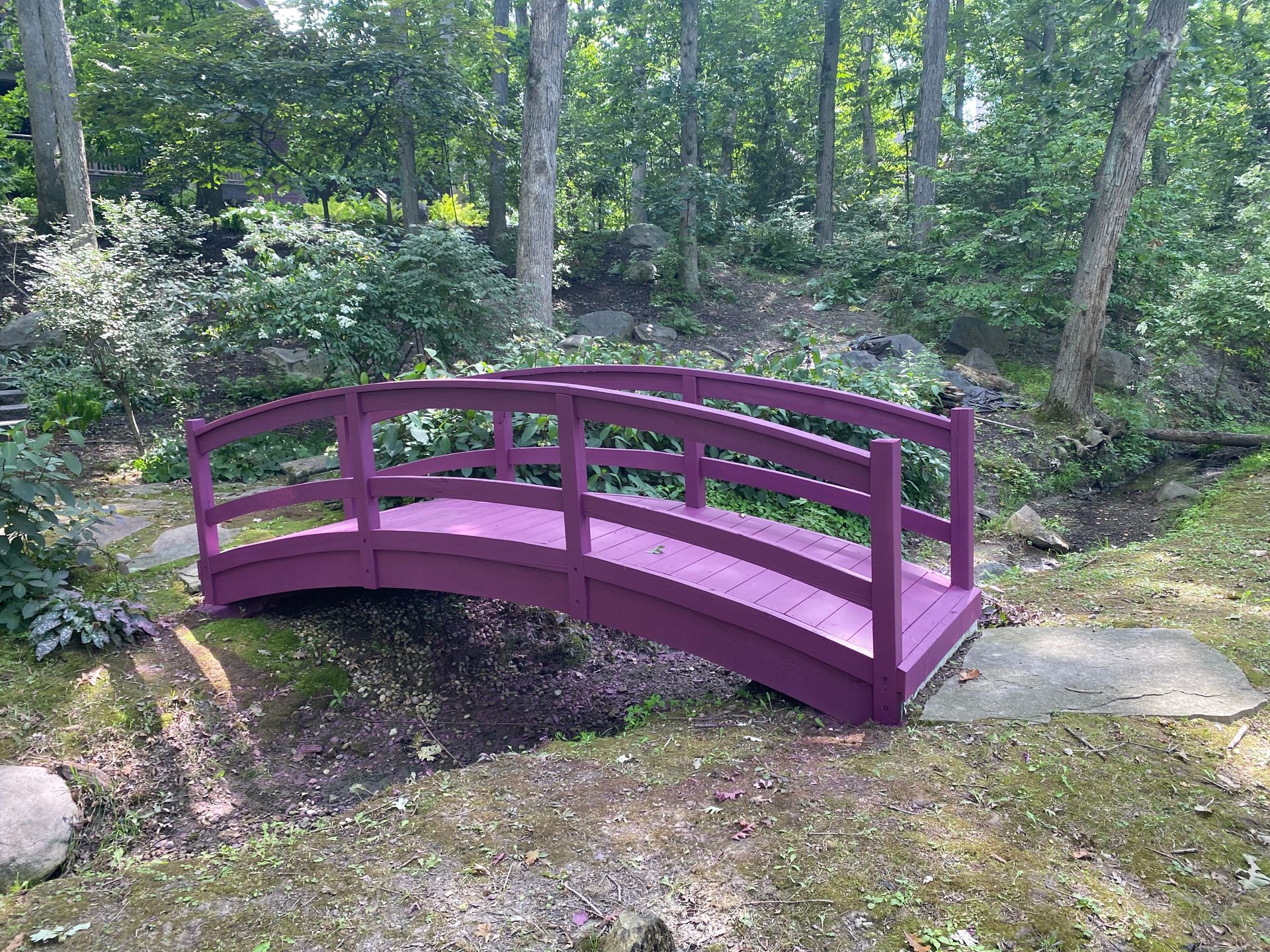 A purple bridge in the middle of a forest.