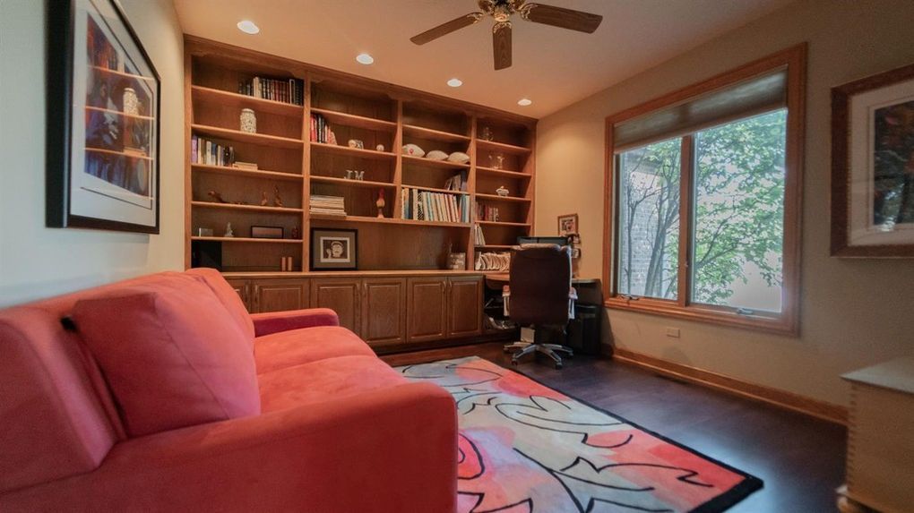 A living room with a red couch , chair , desk and ceiling fan.
