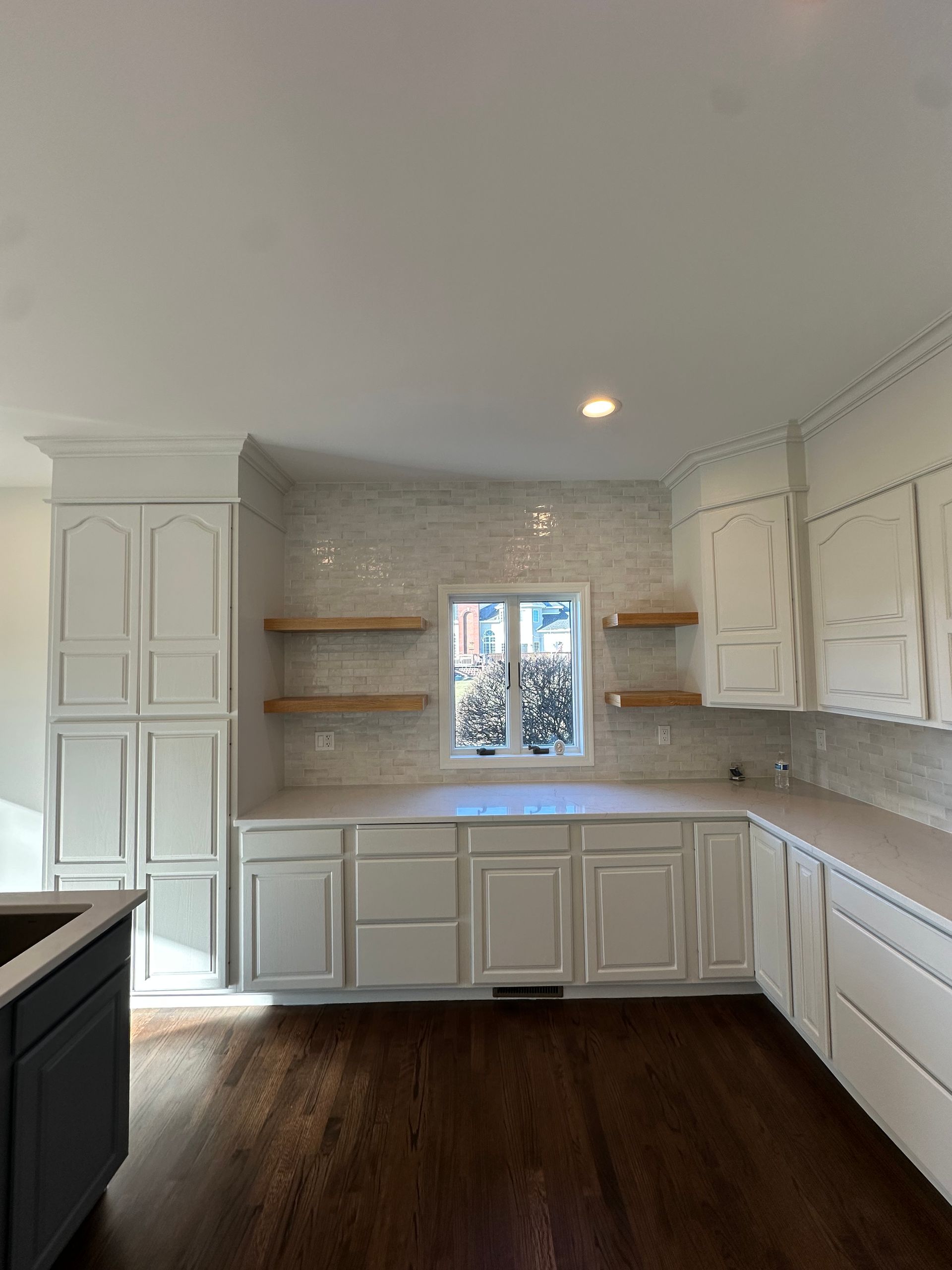 A kitchen with white cabinets and hardwood floors and a window.
