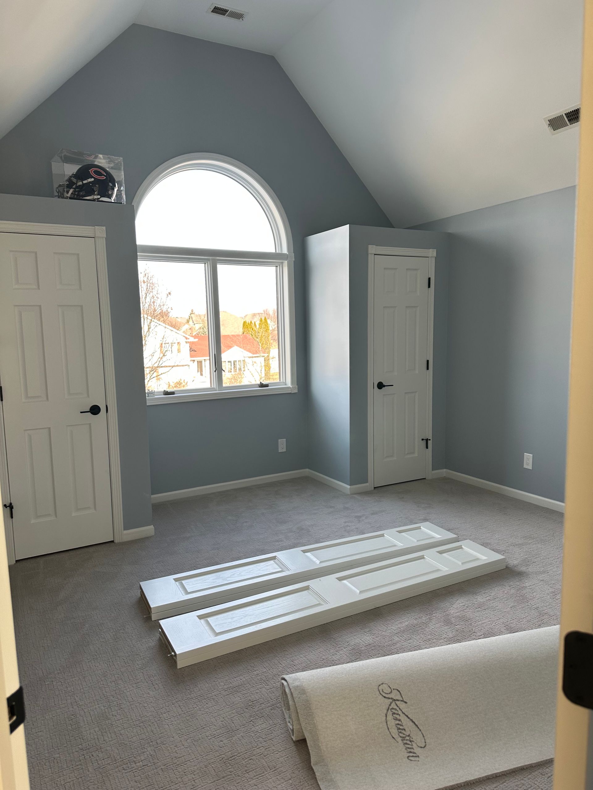 A bedroom with a vaulted ceiling and a large window.