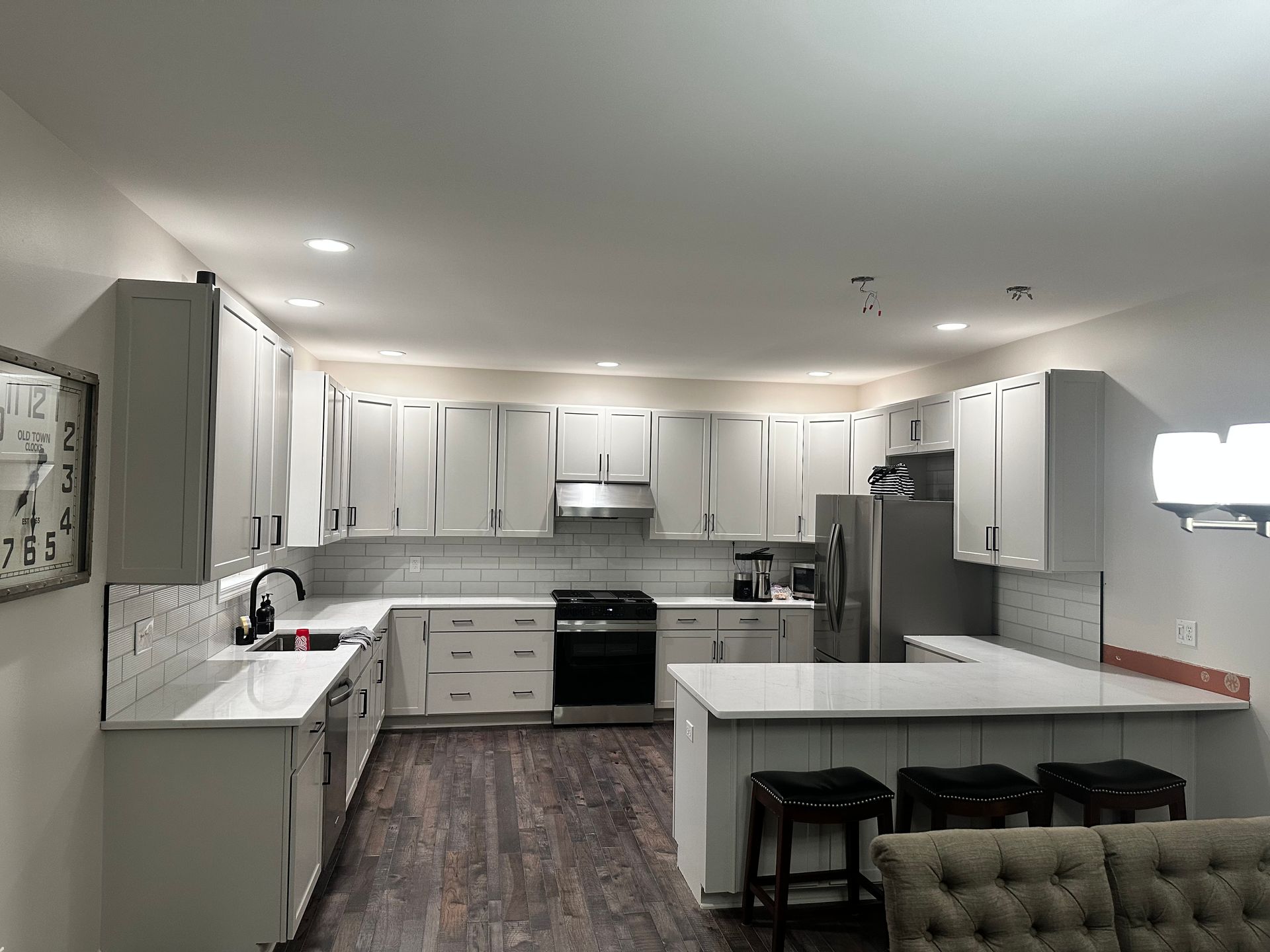 A kitchen with white cabinets , stainless steel appliances , a refrigerator , and a couch.