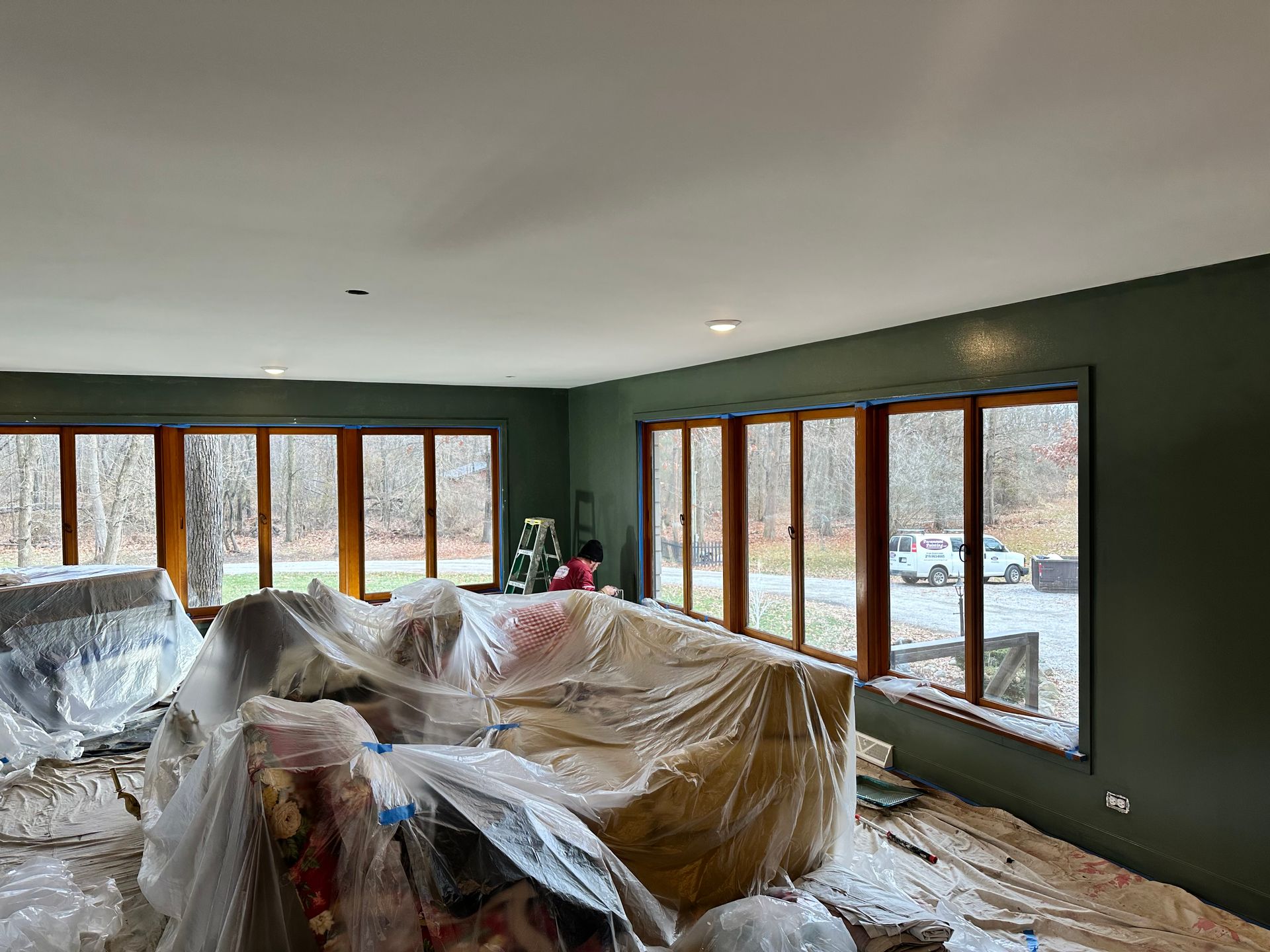 A living room with a couch covered in plastic and a lot of windows.