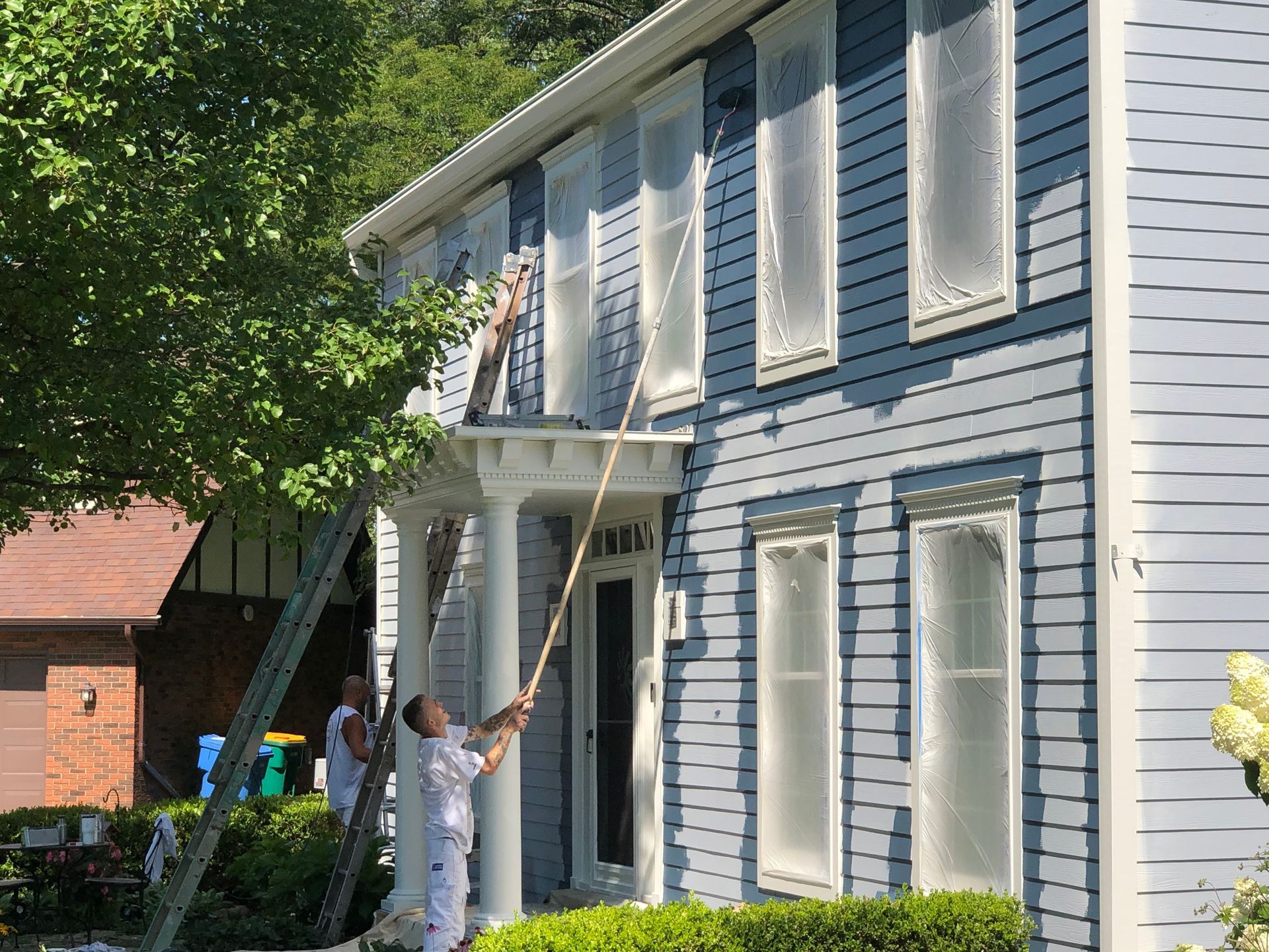 A man is painting a blue house with a ladder