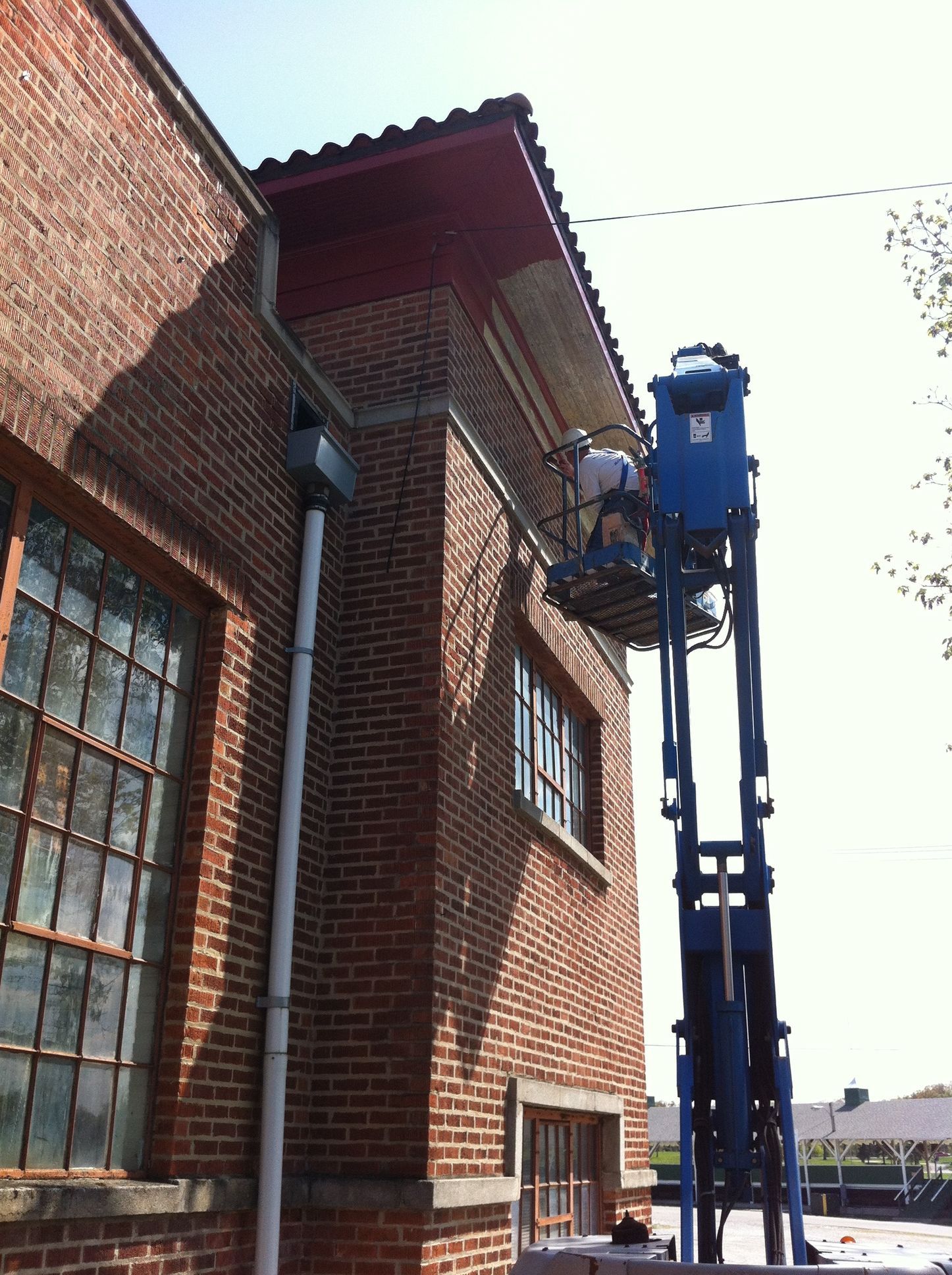 A brick building is being painted by a man on a lift