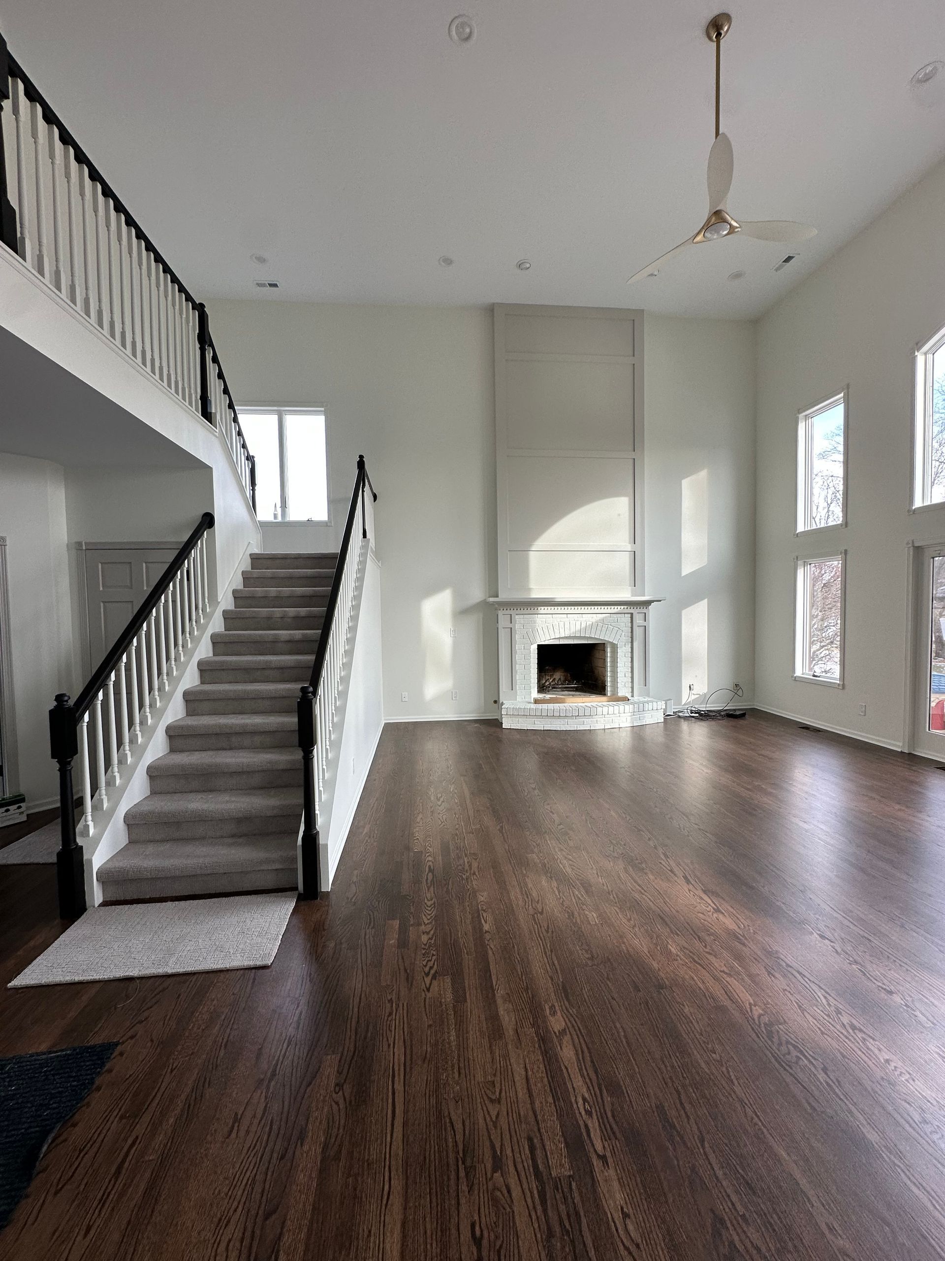An empty living room with hardwood floors , stairs , a fireplace and a ceiling fan.