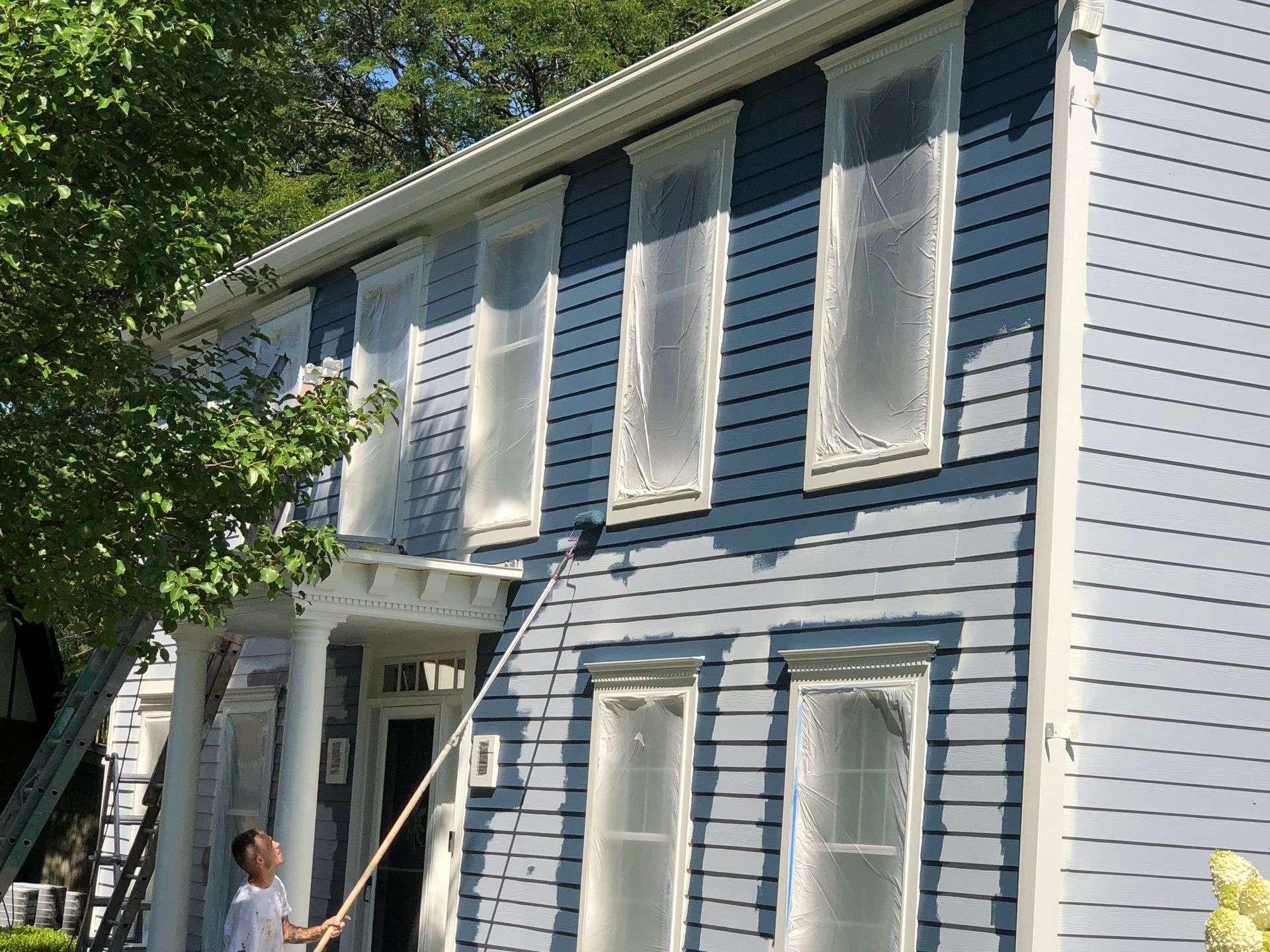 A man is cleaning a blue house with a long pole.