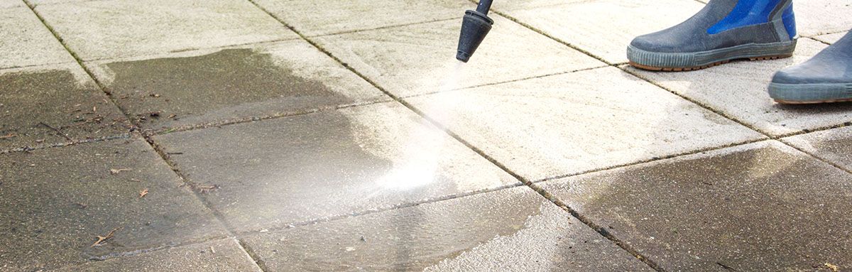 A person is cleaning a sidewalk with a pressure washer