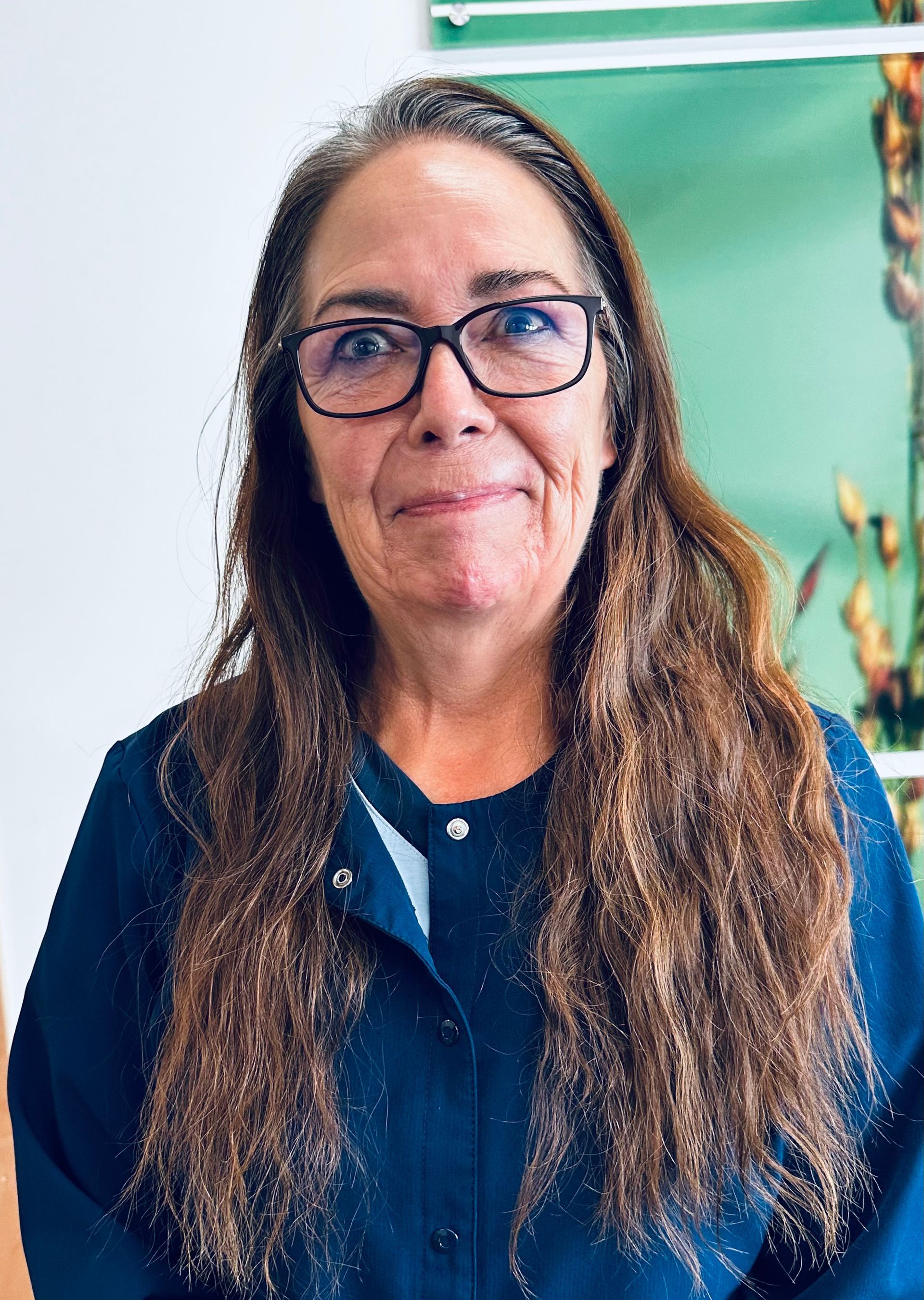 A woman wearing glasses and a blue jacket is smiling for the camera.