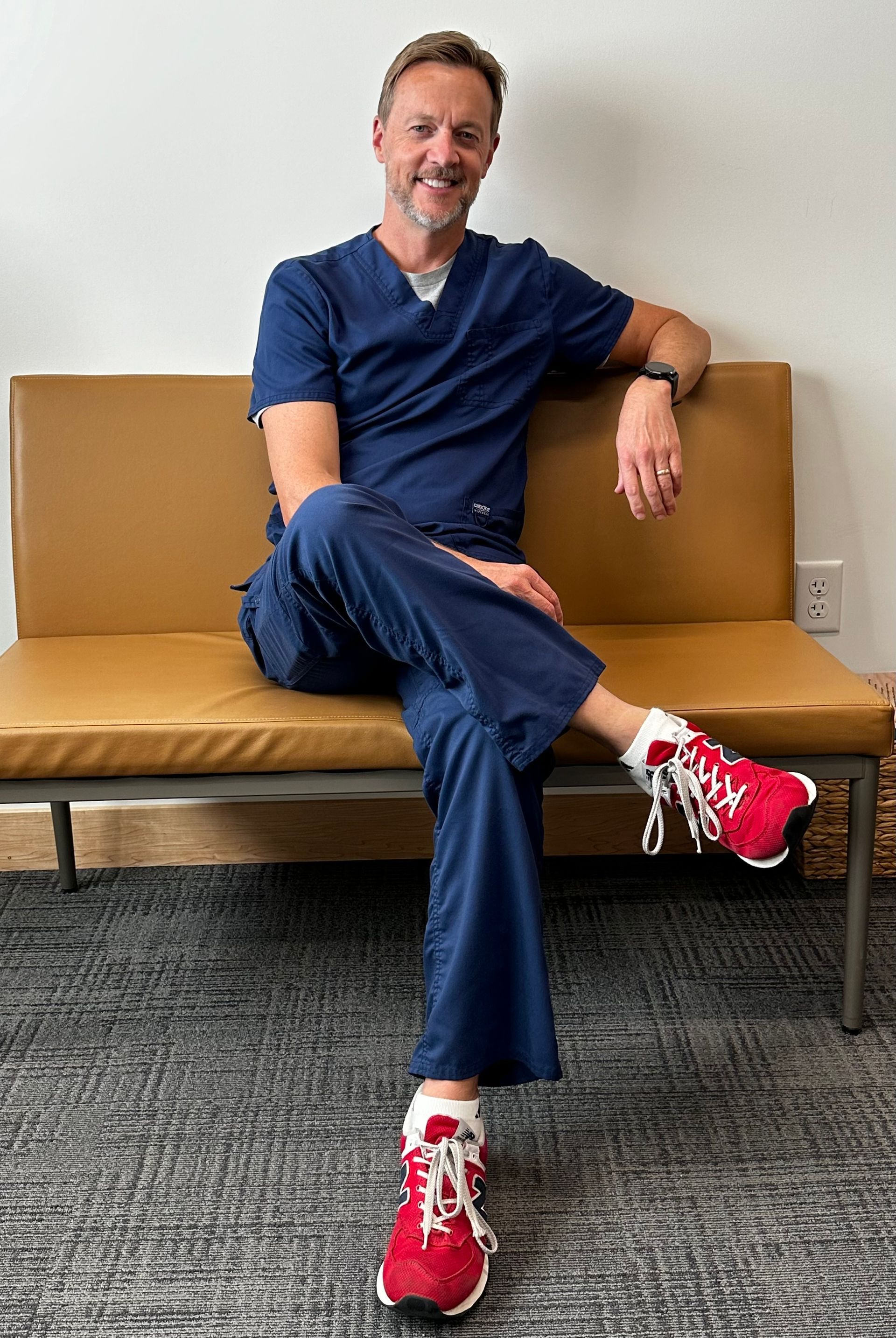 A man in scrubs is sitting on a couch wearing red sneakers.