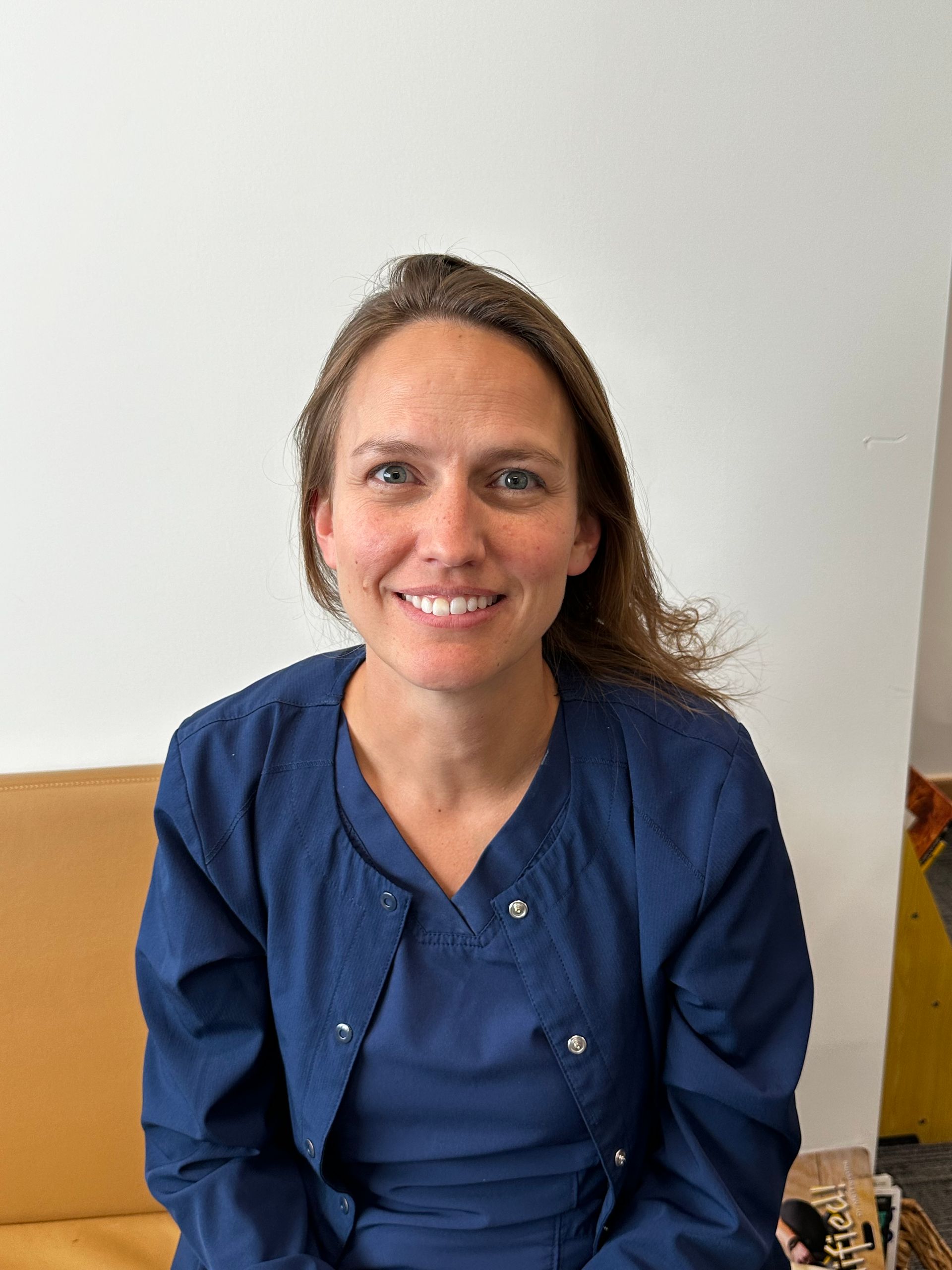 A woman in a blue shirt is smiling while sitting on a couch.