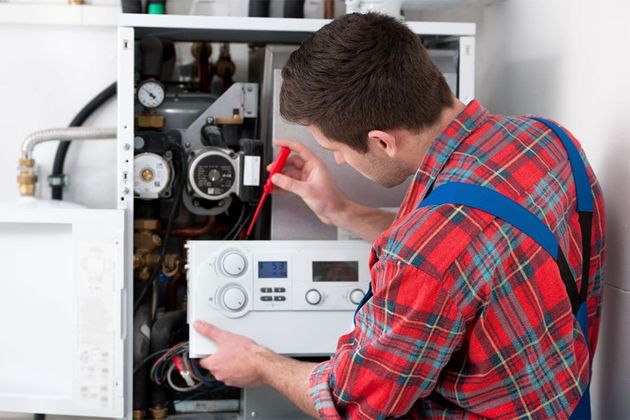 Technician inspecting a boiler with a red screwdriver in an open utility cabinet