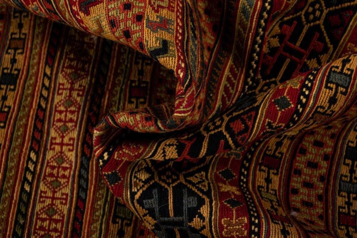 Close-up of a folded woven rug with intricate patterns in red, gold, black, and blue.