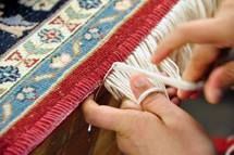 Hands tying fringe on a red and blue patterned rug.