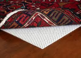 Red patterned rug lifted to show a white textured rug pad on a wooden floor.