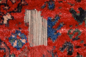 Close-up of a damaged red rug with a large tear exposing white foundation threads.