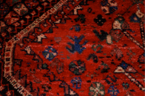 Close-up of a red Persian rug with a geometric pattern, featuring blue and white accents.