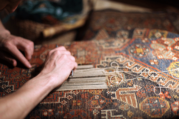 Hands restoring a patterned rug, threading and repairing damage.