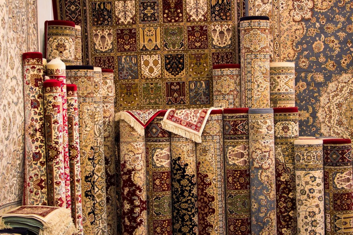 Rolled ornate rugs of various sizes, with intricate patterns, on display in a shop.