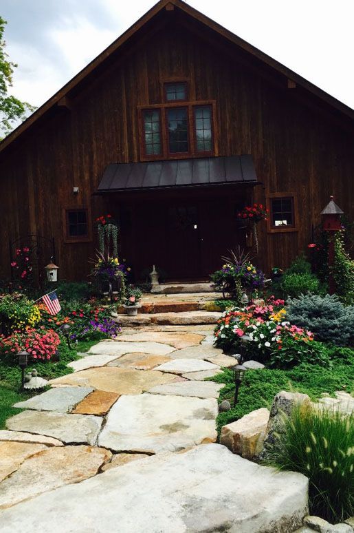 a stone walkway leading to a large wooden barn surrounded by flowers .