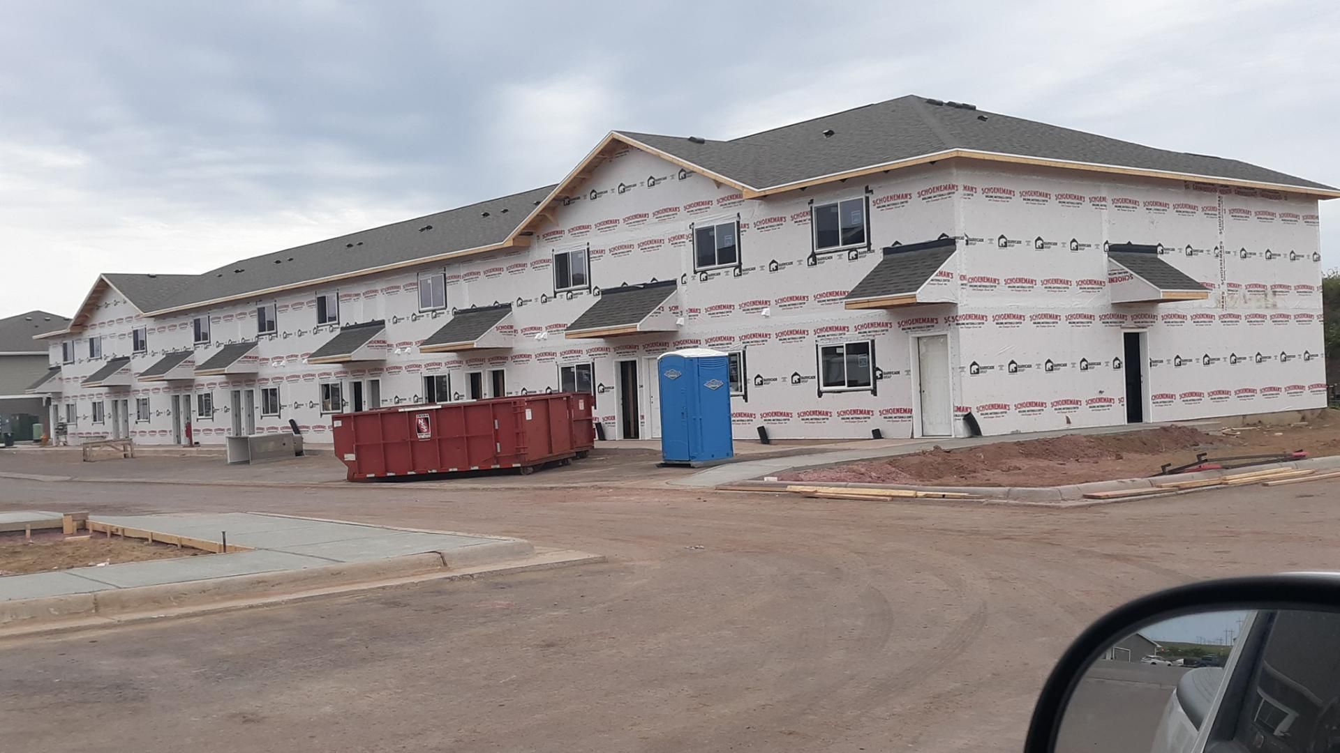 A building under construction with a blue dumpster in front of it.