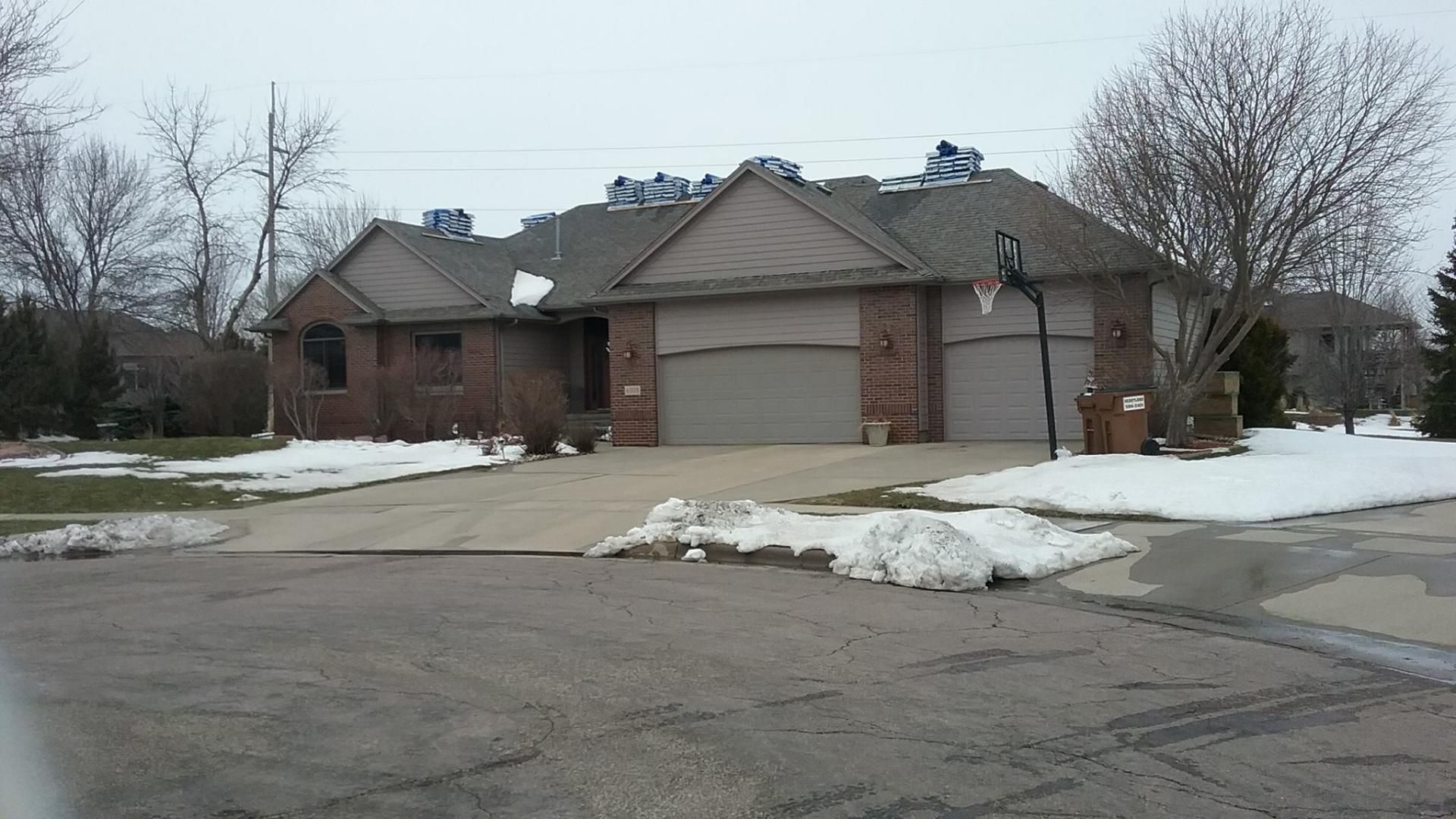 A brick house with two garages and a snowy driveway