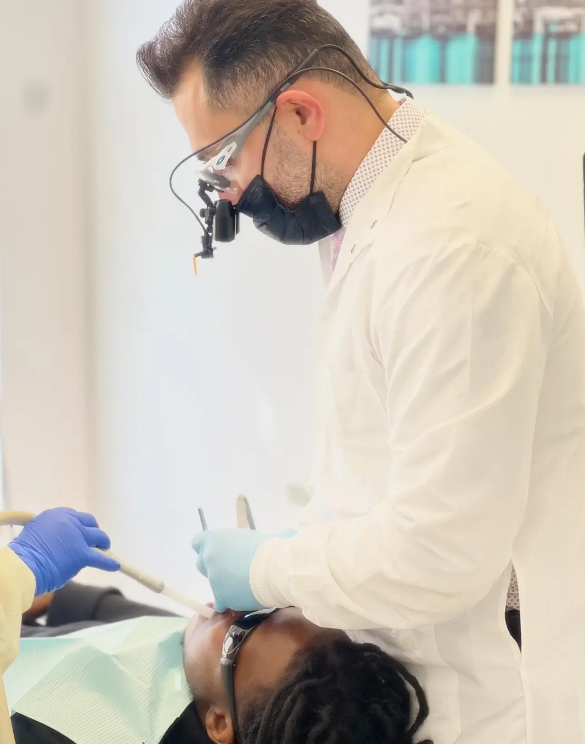 A dentist wearing a mask and glasses examines a patient 's teeth.