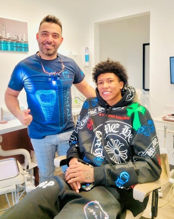 A man is standing next to a young man sitting in a dental chair.