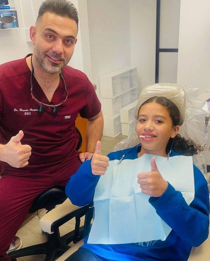 A dentist and a little girl are giving a thumbs up