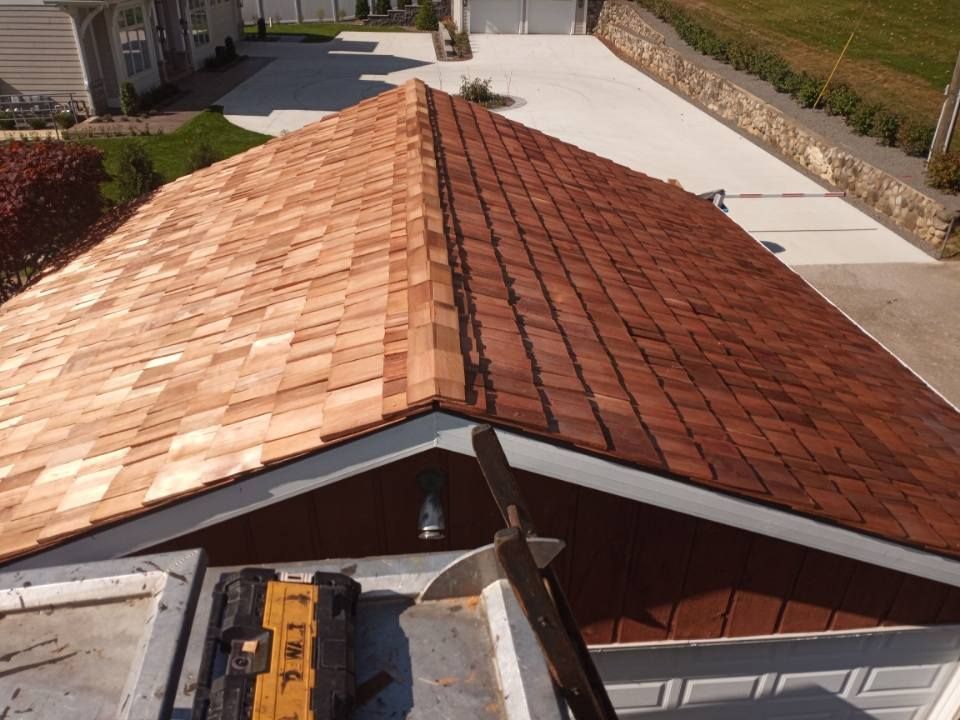 New cedar shake roof installation on a brown building; tools in the foreground.