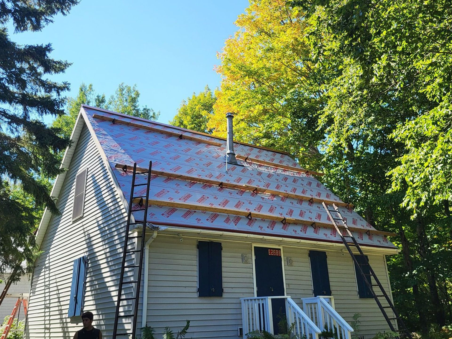 House with a partially installed silver metal roof; two ladders leaning on the roof.