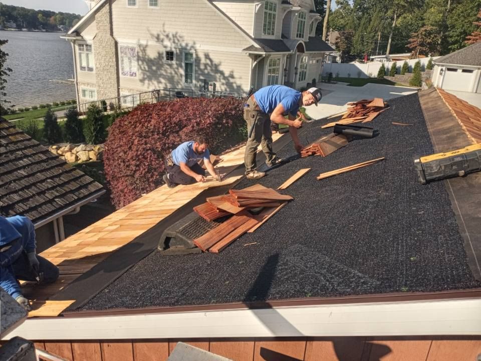 Roofers installing wooden shingles on a house roof near a lake.