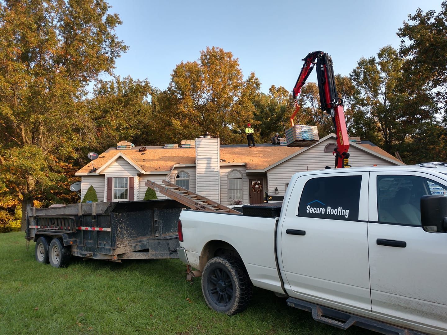 A white truck with a crane attached to it is parked in front of a house.