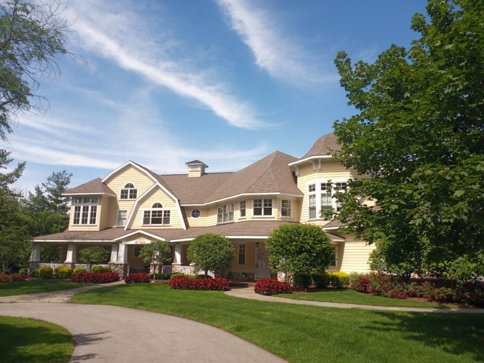 A large yellow house with a brown roof is surrounded by trees