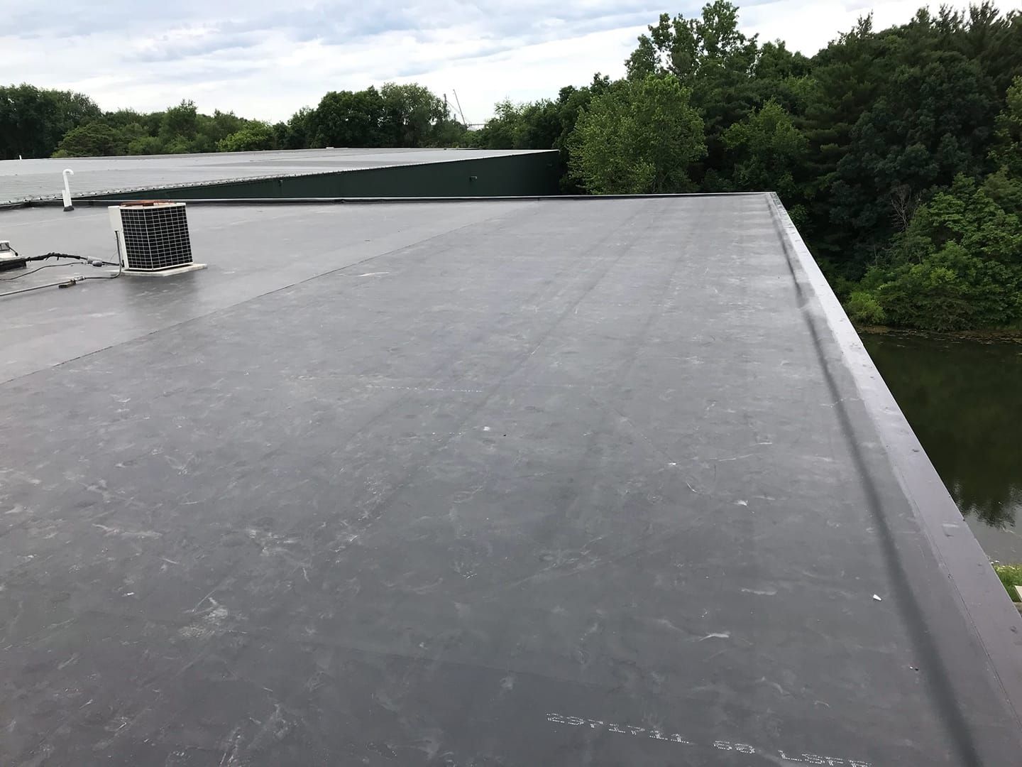 A black roof with a chimney on top of it and trees in the background.