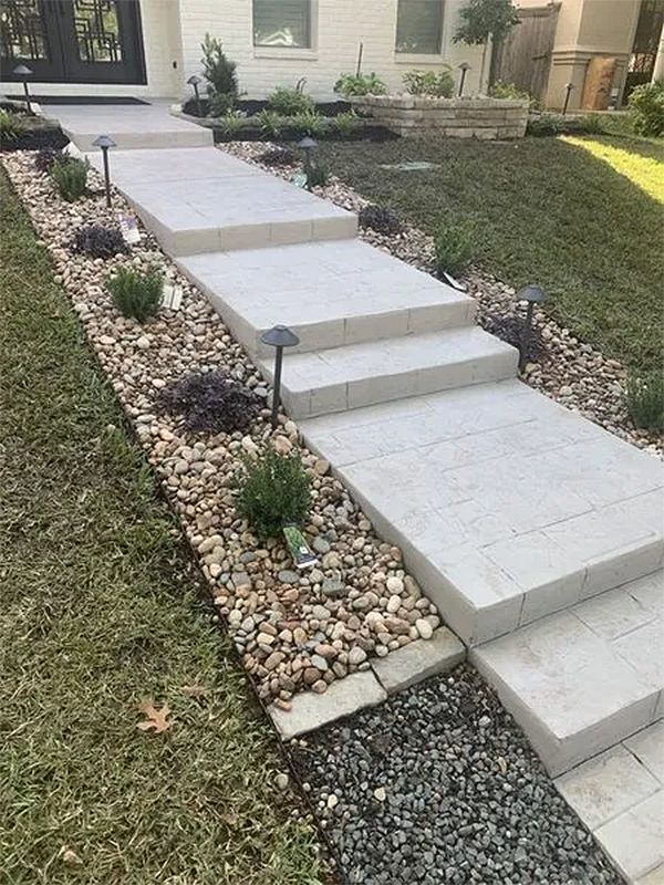Front yard concrete walkway with steps, bordered by gravel, leading up to a house entrance