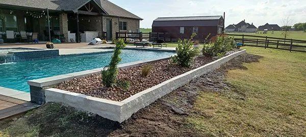 Backyard pool beside a raised flower bed and lawn near a house and fence