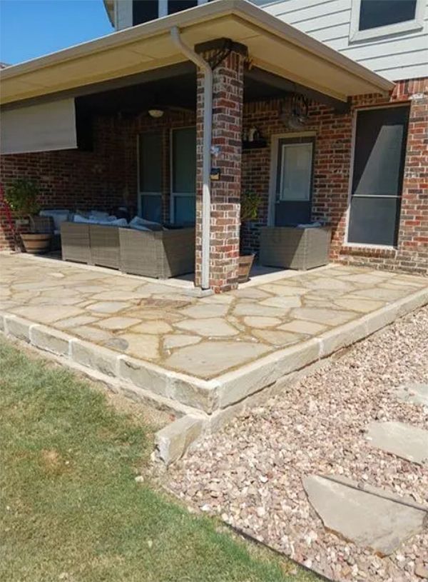 Front porch with brick columns, stone patio, and seating area beside a house.