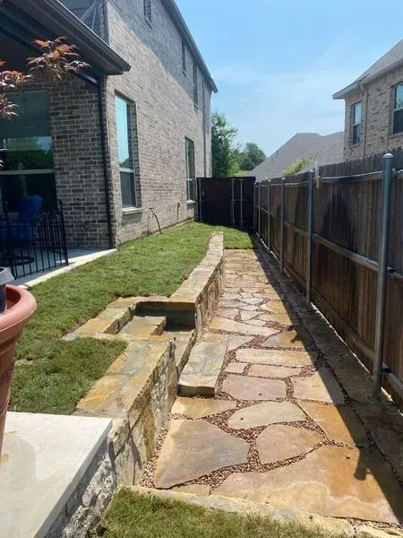 Stone garden path beside brick houses with wooden fence and grassy raised bed