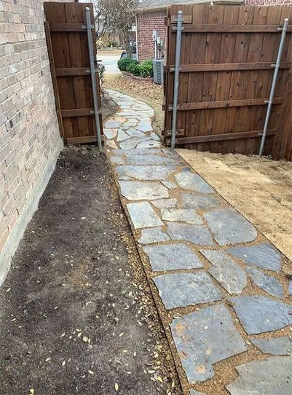 Stone garden path between wooden gates beside a brick wall and bare soil beds