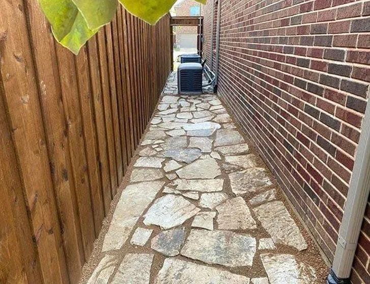 Narrow stone walkway between a wooden fence and brick wall, leading to a gate