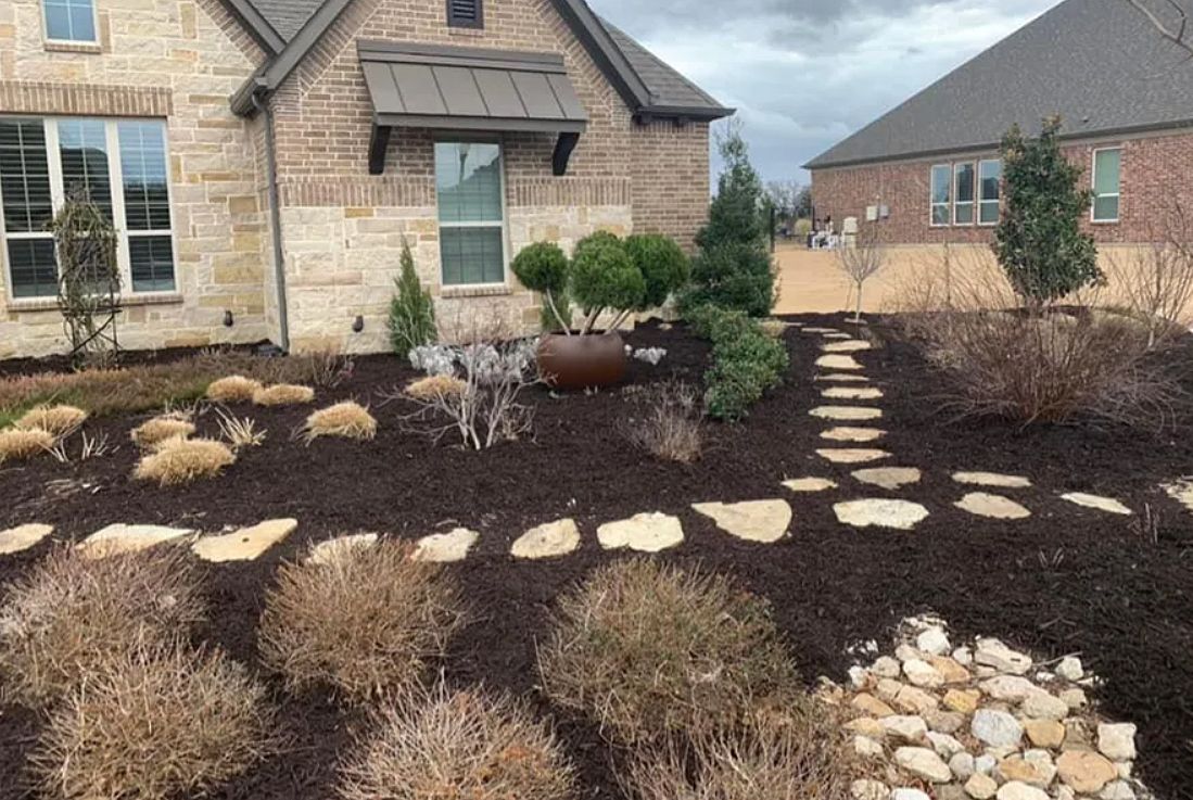 Landscaped front yard with stepping stones, shrubs, and a stone house in the background
