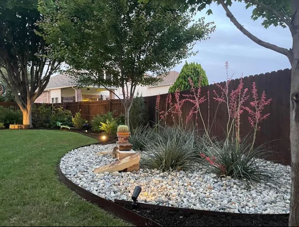Landscaped front yard with curved white rocks, ornamental plants, trees, and a small fountain feature