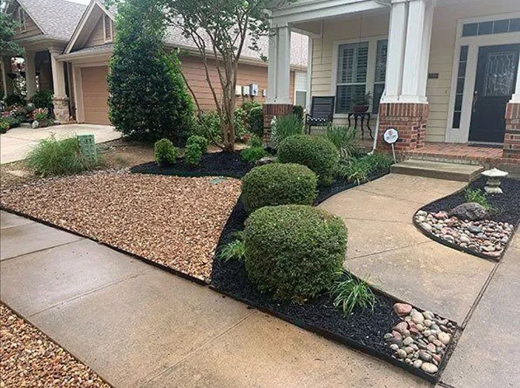 Front walkway with trimmed shrubs, mulch beds, and stone borders outside a house with white columns