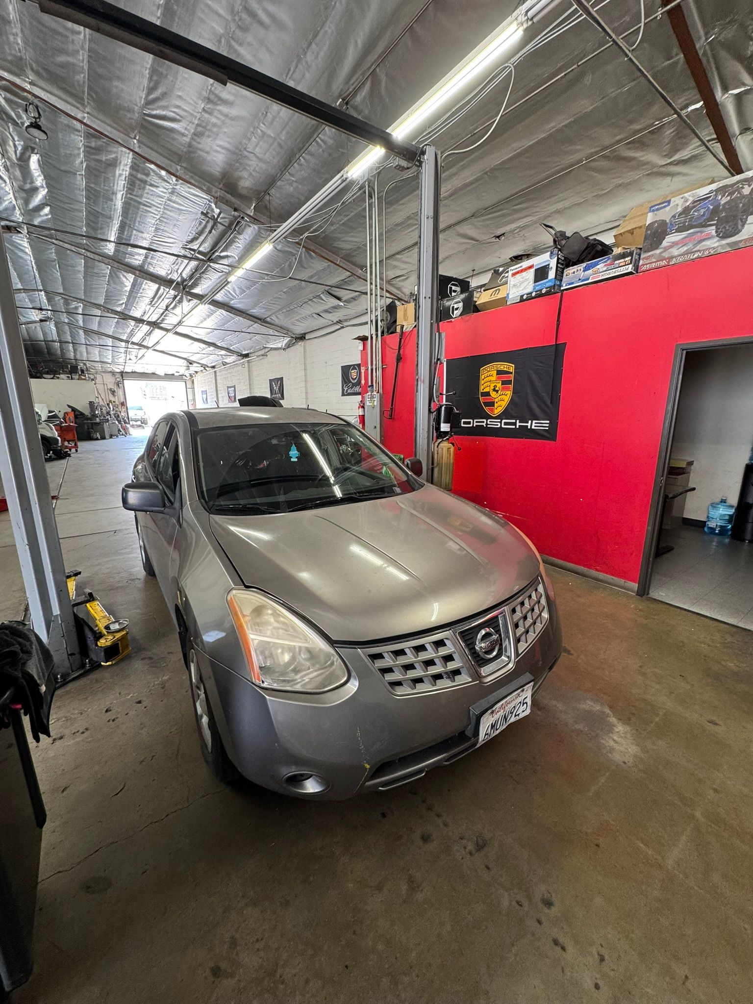 Silver minivan in an auto shop bay with a red wall and lifts in the background