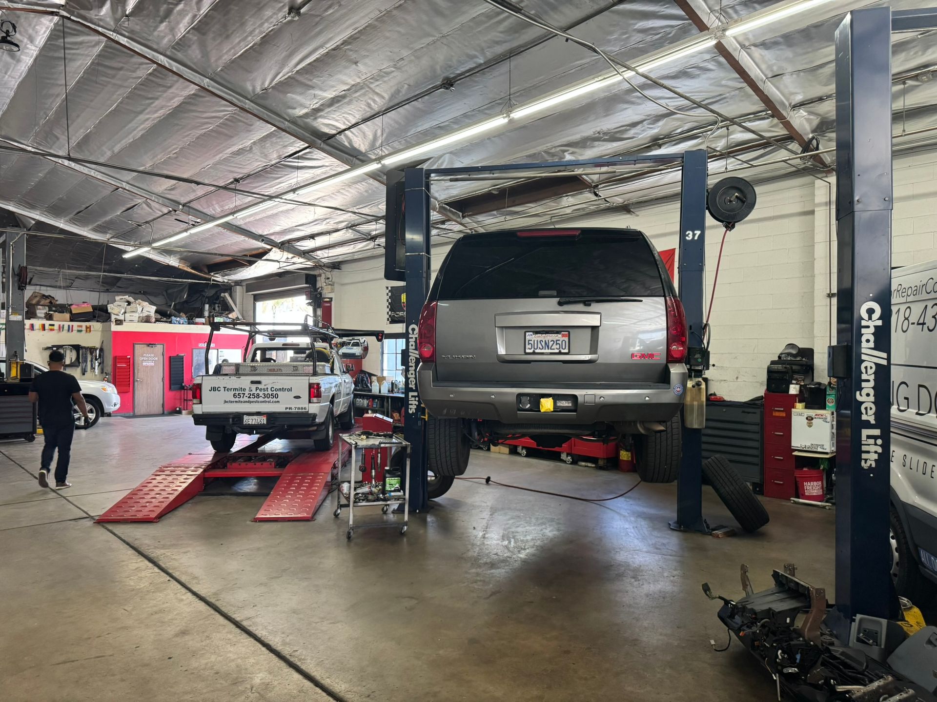 Auto repair shop with a lifted gray SUV on a hydraulic lift and a white pickup on ramps.