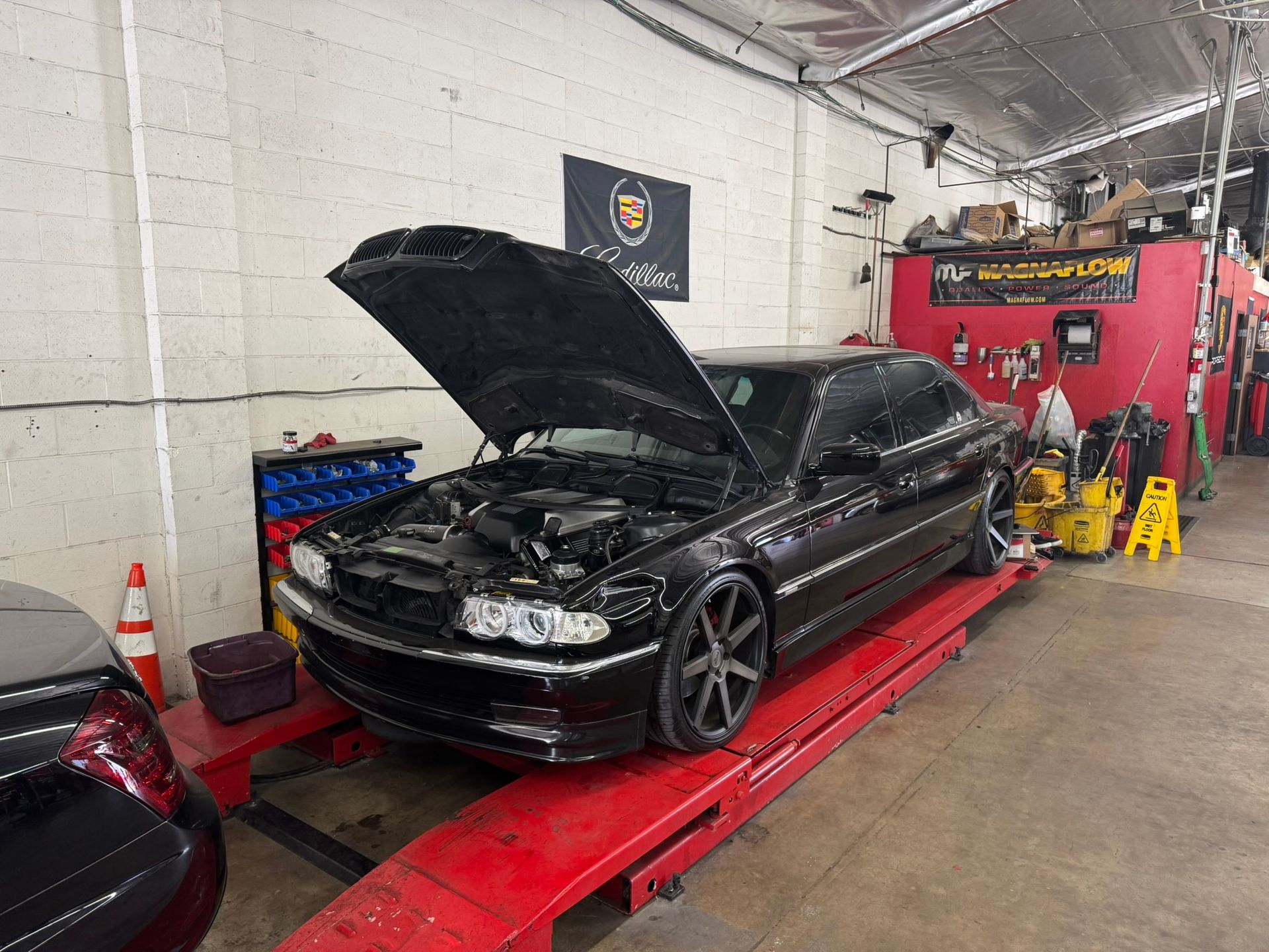 Black car with hood open on a red lift inside an auto repair shop