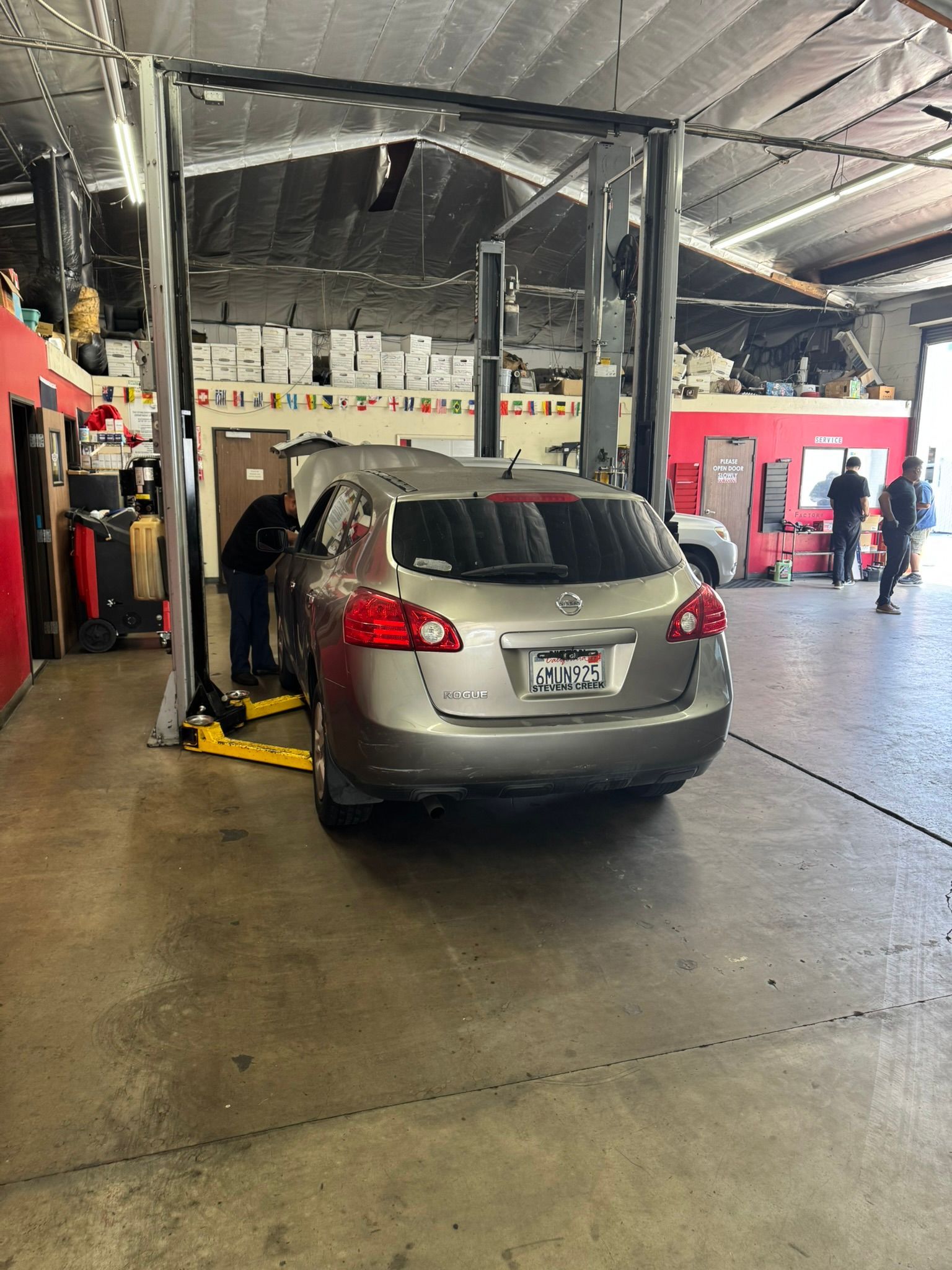 Gray hatchback in a garage with a car lift, viewed from the rear.