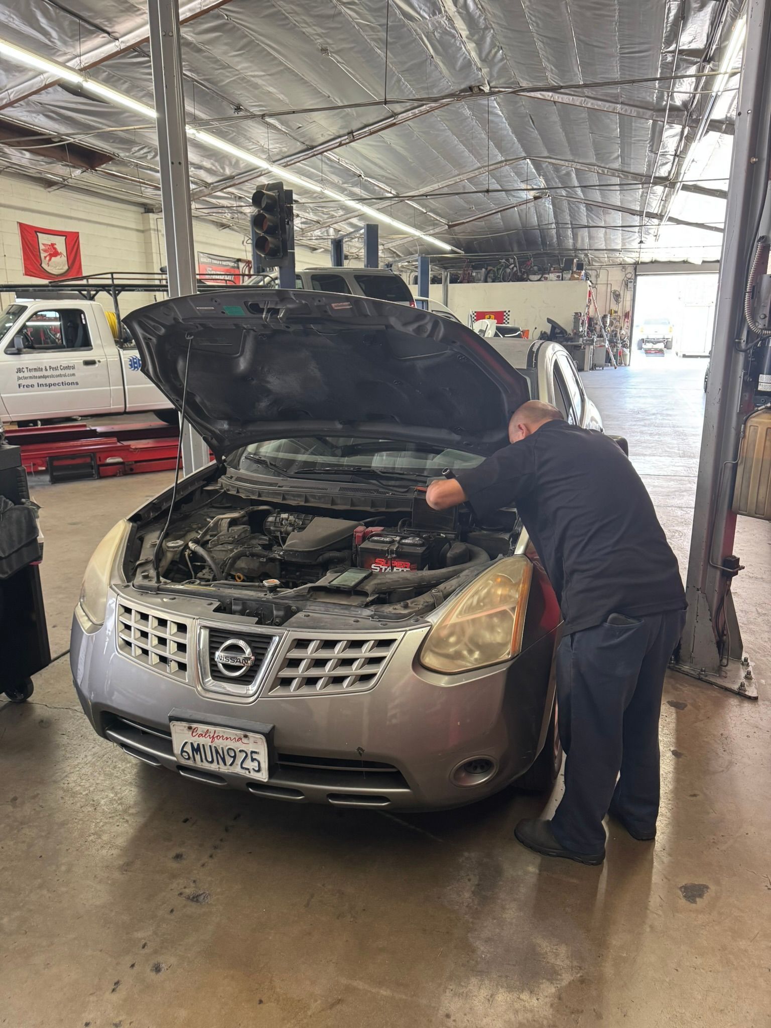 Mechanic checking a silver car with open hood in an auto repair shop
